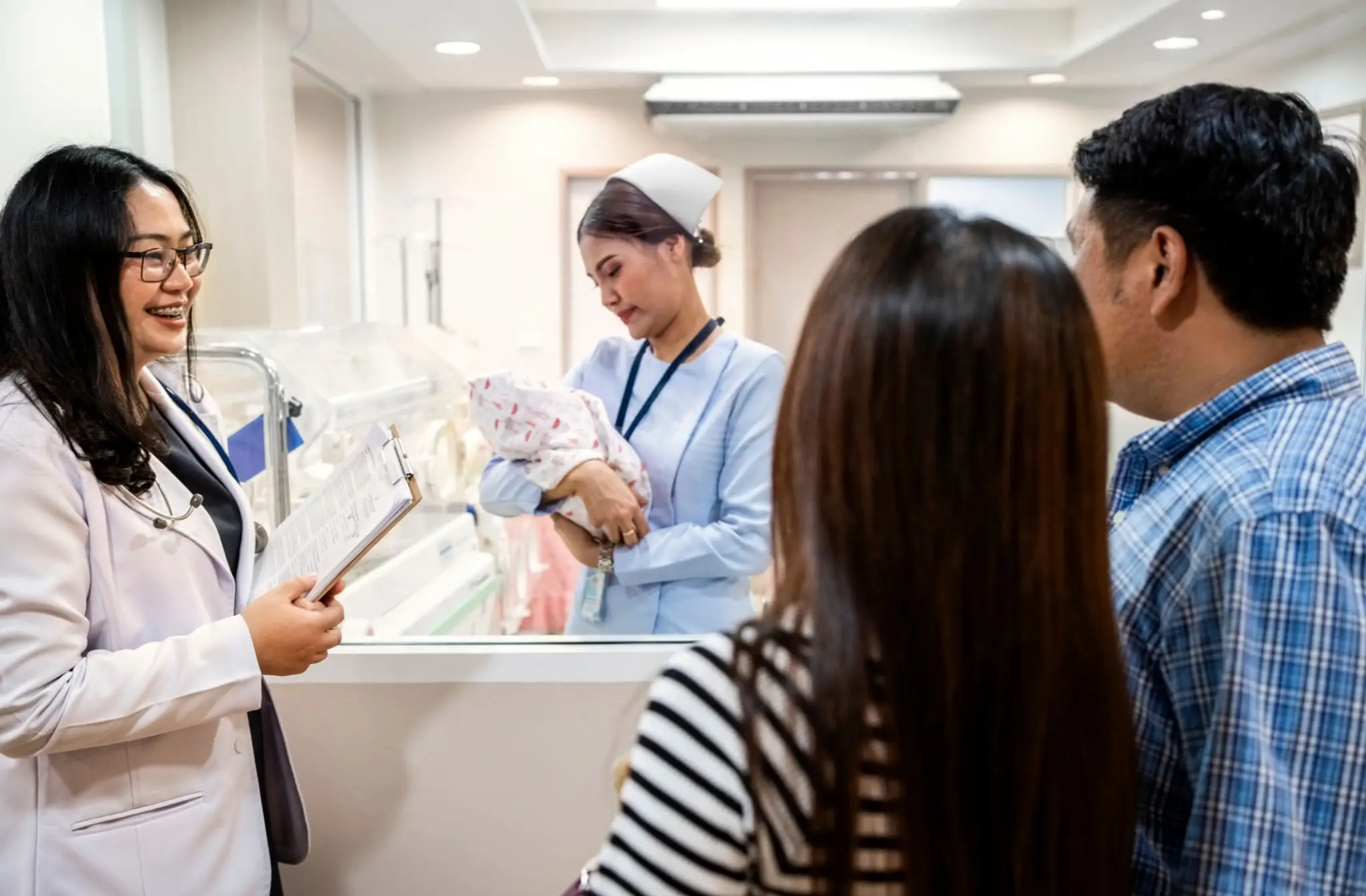 Medical staff explain newborn care to new parents in hospital nursery.