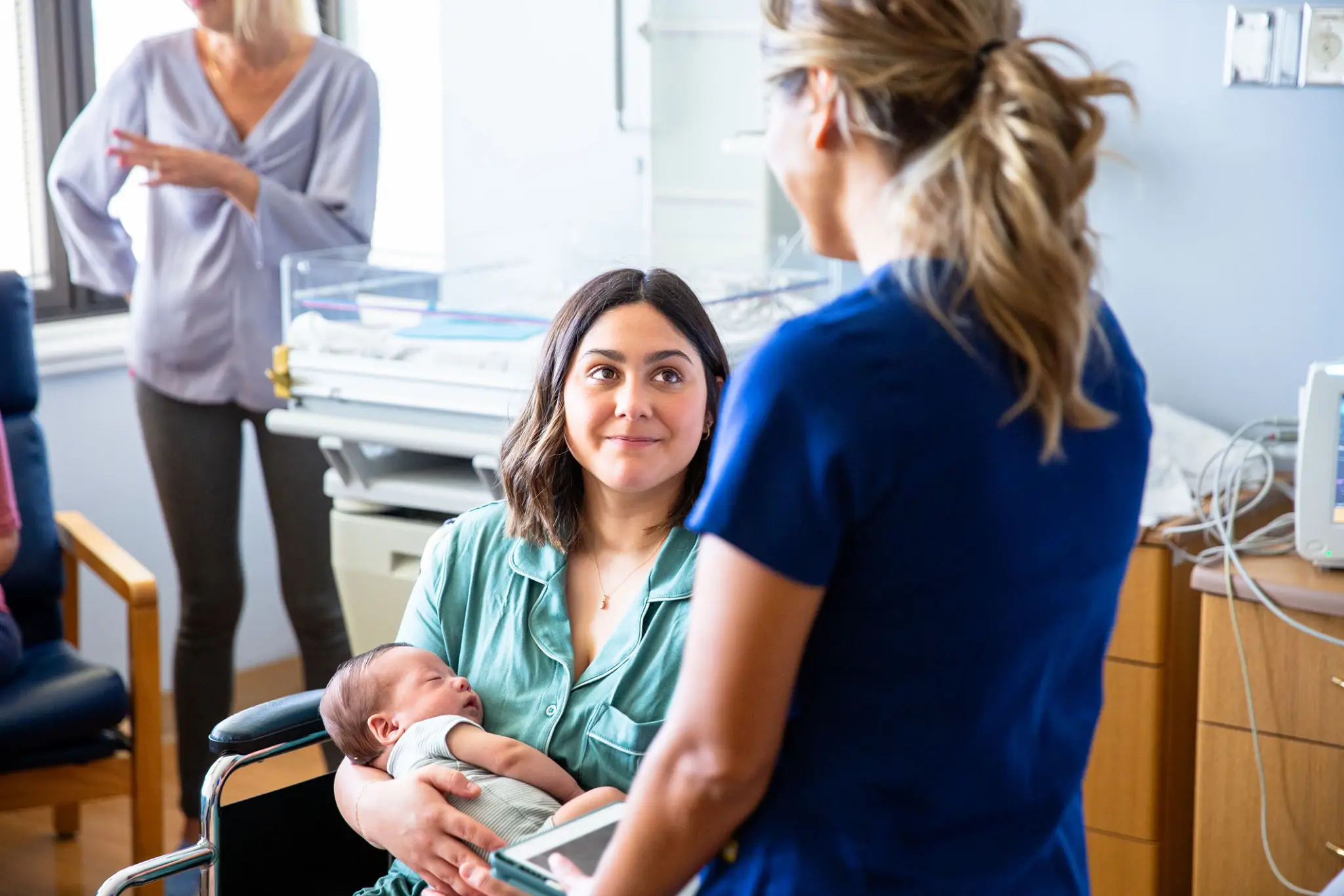 A mother breastfeeding her baby while talking to a healthcare professional.