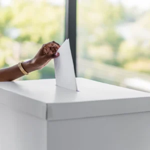 Hand inserting a ballot into a white voting box.