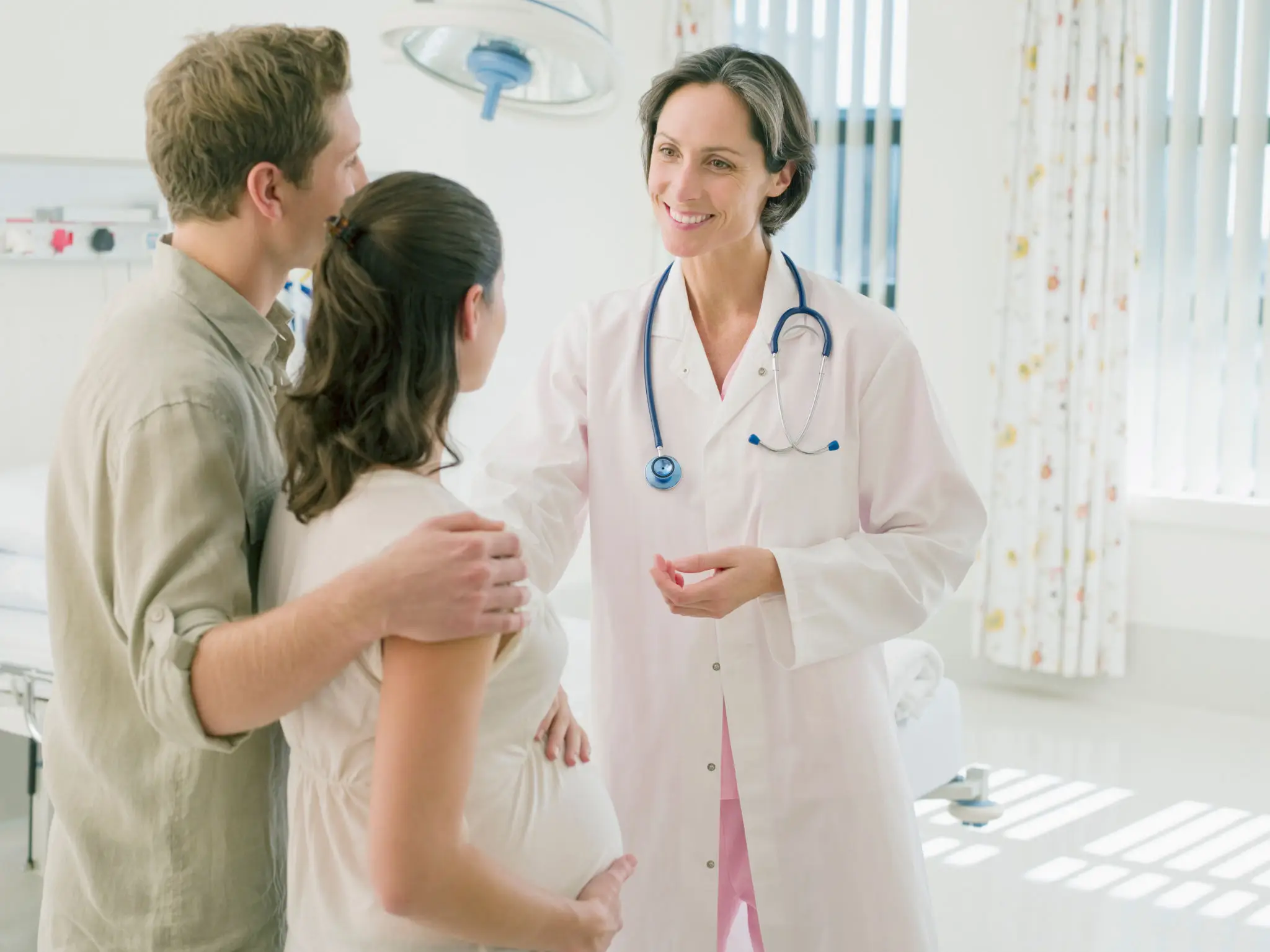 Doctor consulting a pregnant woman with her partner in a hospital room.
